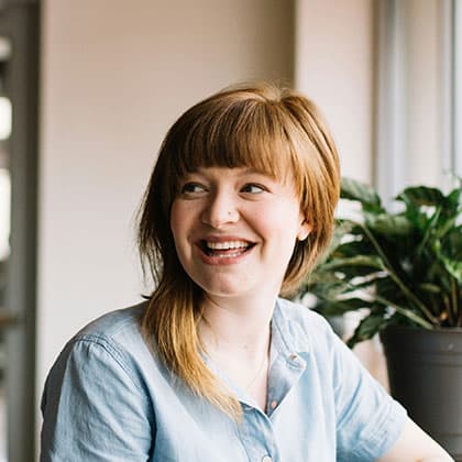 Profesional comprometida con la atención y la experiencia del cliente Mujer sonriendo en oficina con luz natural y planta decorativa